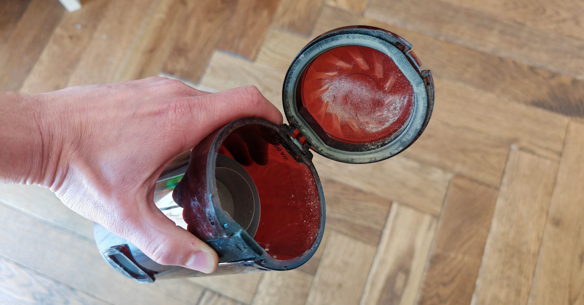 Pour vider le collecteur, il est necessaire de le retirer du corps de l'aspirateur et d'appuyer la gachette noire pour que la trape s'ouvre. (c) Labo Maison