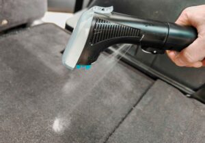Poignée d'un injecteur-extracteur en action, pulvérisant de l'eau et du produit pour nettoyer un siège de voiture. (c) Labo Maison